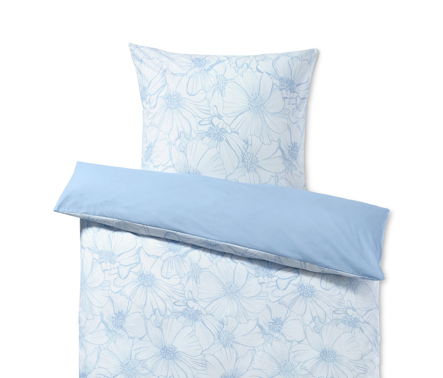 Blaue Renforcé-Bettwäsche mit Blumenmuster auf einem Bett.