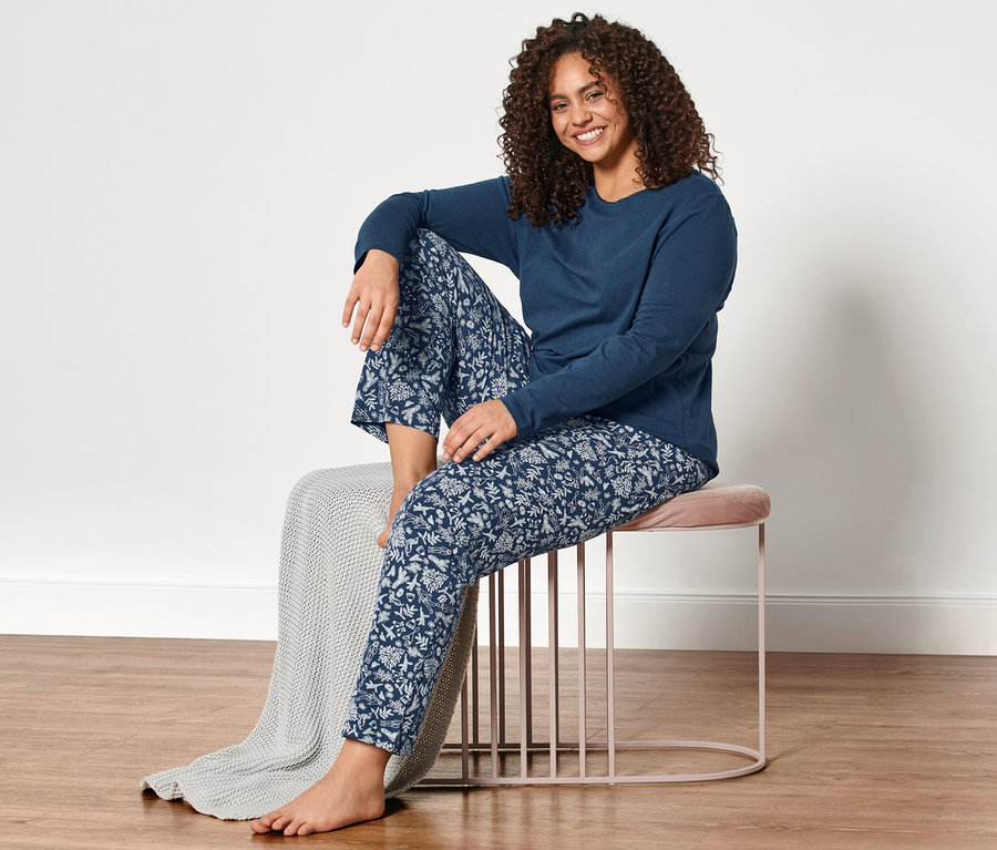 Frau sitzt in blauem Pyjama auf einem Hocker.