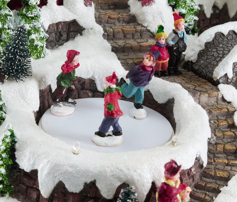 Figuren laufen Schlittschuh auf einer Eisbahn in einem verschneiten Luville – Bergdorf mit Kirche.