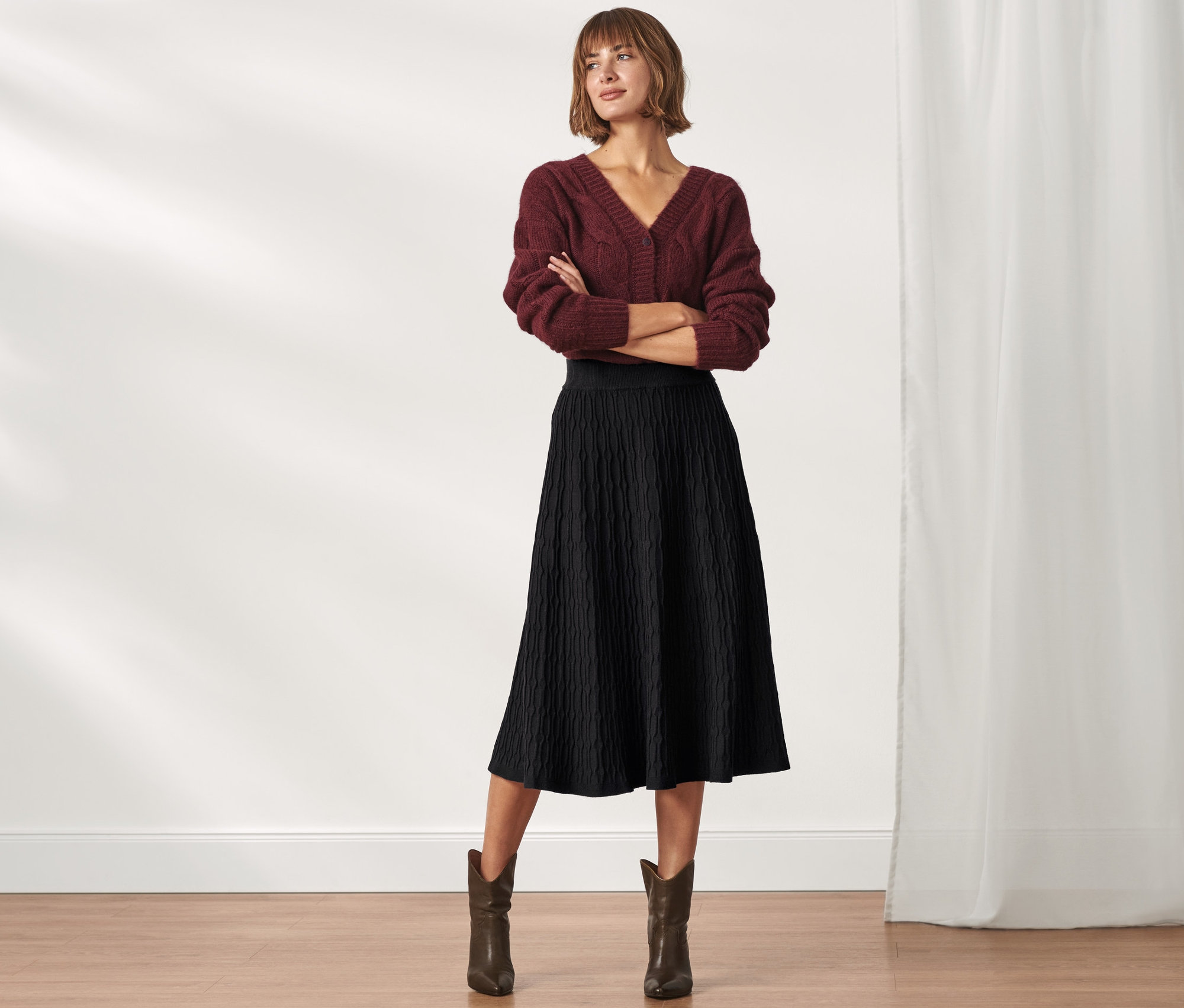 Frau posiert in bordeauxfarbenem Pullover und schwarzem Strickrock in Midi-Länge.