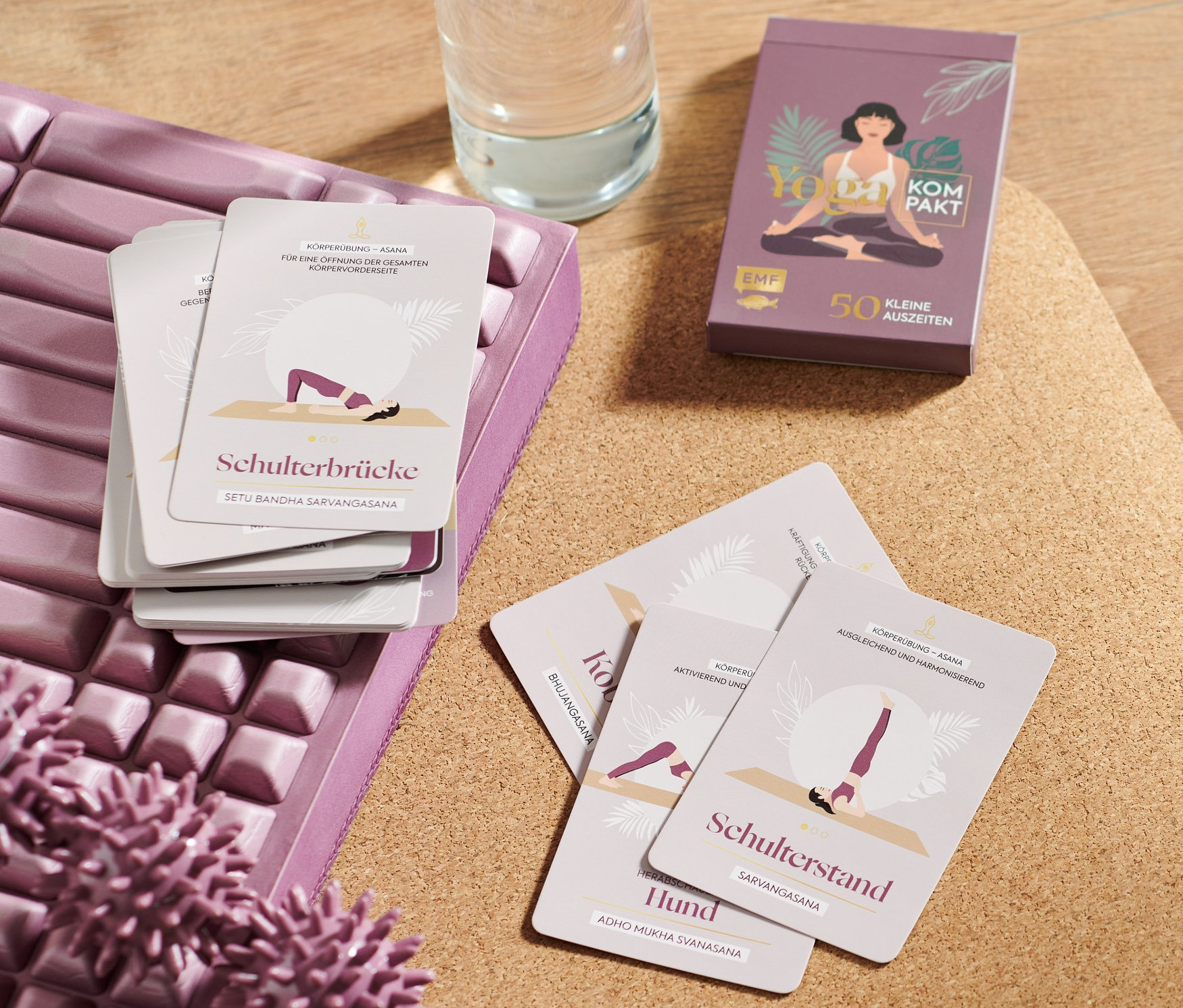 Yogamatte, Massagerolle, Wasserflasche und ein Yoga-Karten-Set liegen auf einer Korkmatte.
