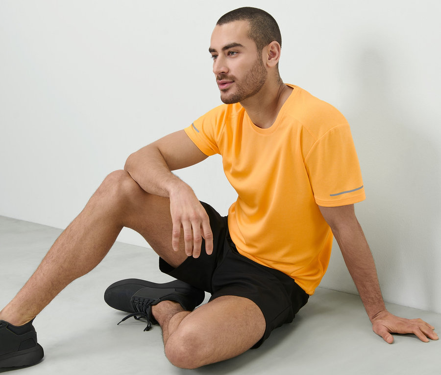Mann sitzt auf dem Boden und trägt ein pfirsichfarbenes Funktionsshirt.