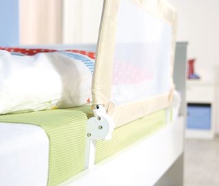 Detailansicht eines beigen roba Bettschutzgitters »Klipp-Klapp«, das an einem weißen Bett befestigt ist.