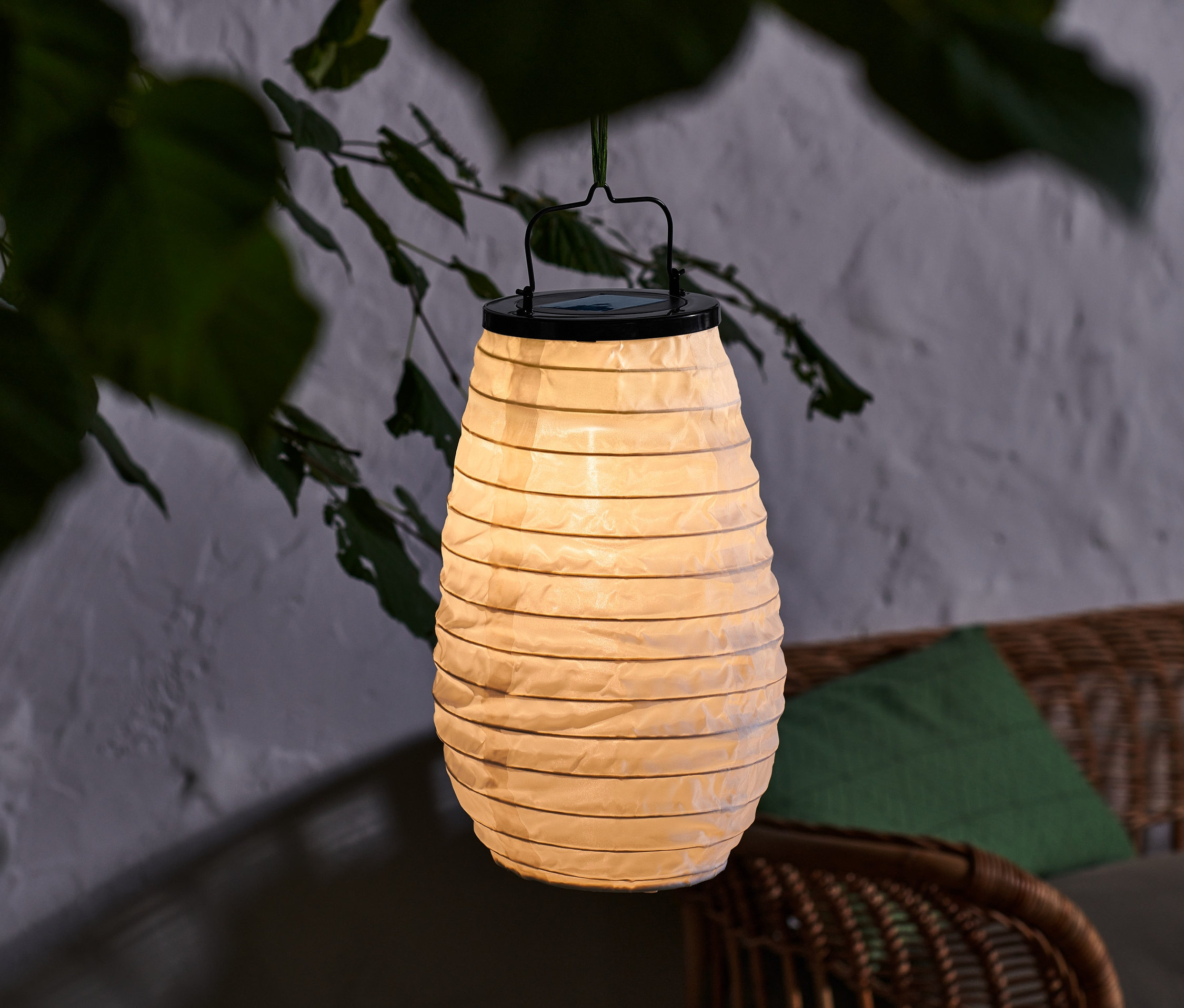 Eine Solar-Lampion mit schwarzem Griff hängt draußen zwischen Ästen.