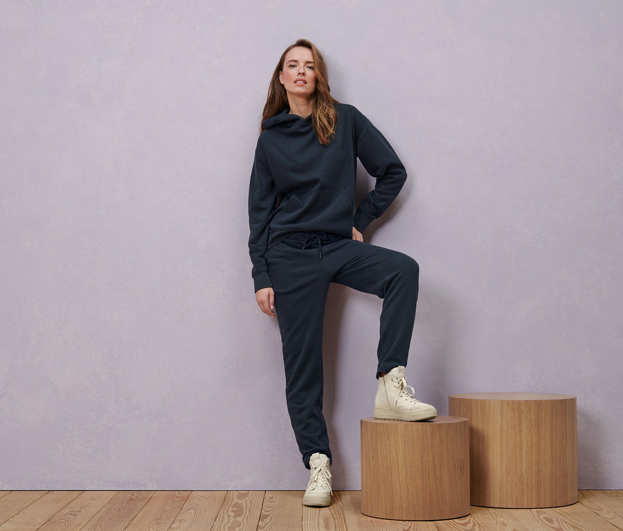 Frau posiert in navy Hoodie, Sweathose und gefütterten Leder-Sneakern.