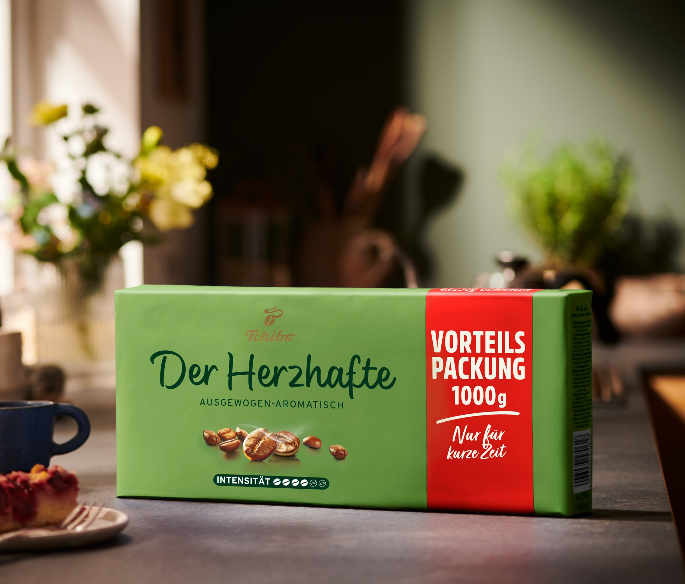 Eine Packung Der Herzhafte Gemahlen Kaffee neben einem Stück Kuchen und einer blauen Tasse.