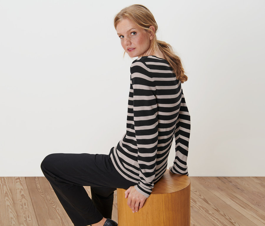 Frau sitzt auf einem Hocker und trägt einen Gestreiften Feinstrickpullover.