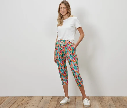 Frau steht und trägt eine mehrfarbige 3/4-Jerseyhose und ein weißes T-Shirt.