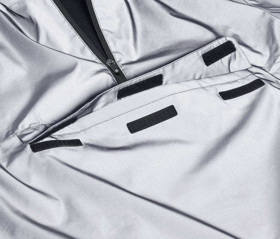 Detailaufnahme eines reflektierenden Windbreakers mit schwarzem Reißverschluss und Tasche.
