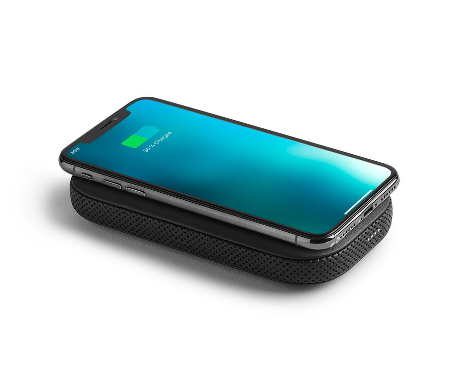 Ein Mobiltelefon wird auf einer schwarzen Powerbank aufgeladen. Auf der Powerbank liegt ein Lexon »POWERSOUND« Lautsprecher.