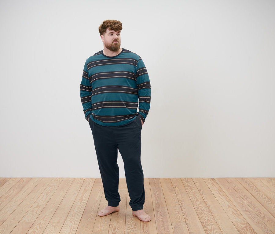 Mann steht mit Händen in den Hosentaschen und trägt einen Pyjama.