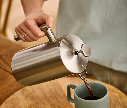 Frau gießt Kaffee aus einer doppelwandigen Siebstempelkanne aus Edelstahl mit 900 ml in eine Tasse.