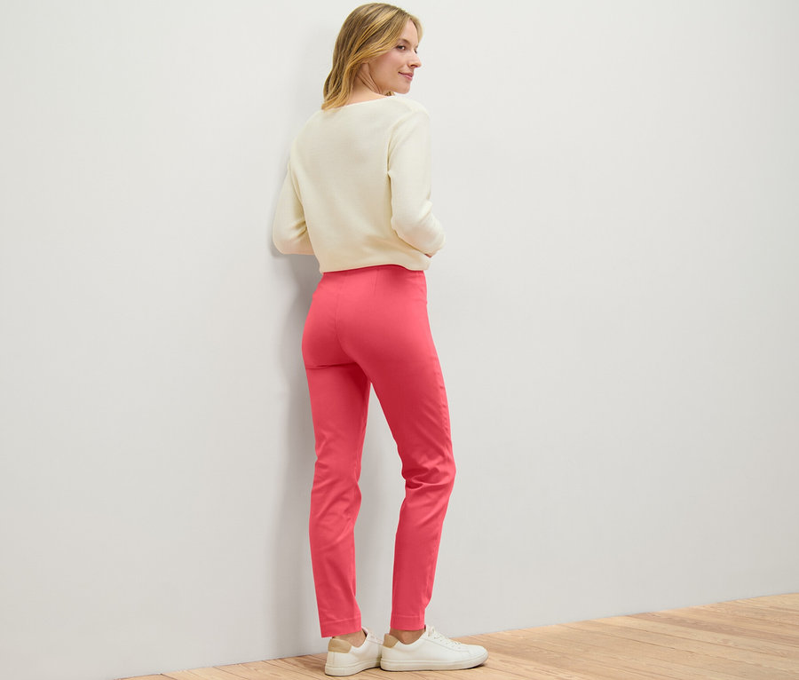 Frau blickt über die Schulter und trägt eine korallfarbene Stretchhose.