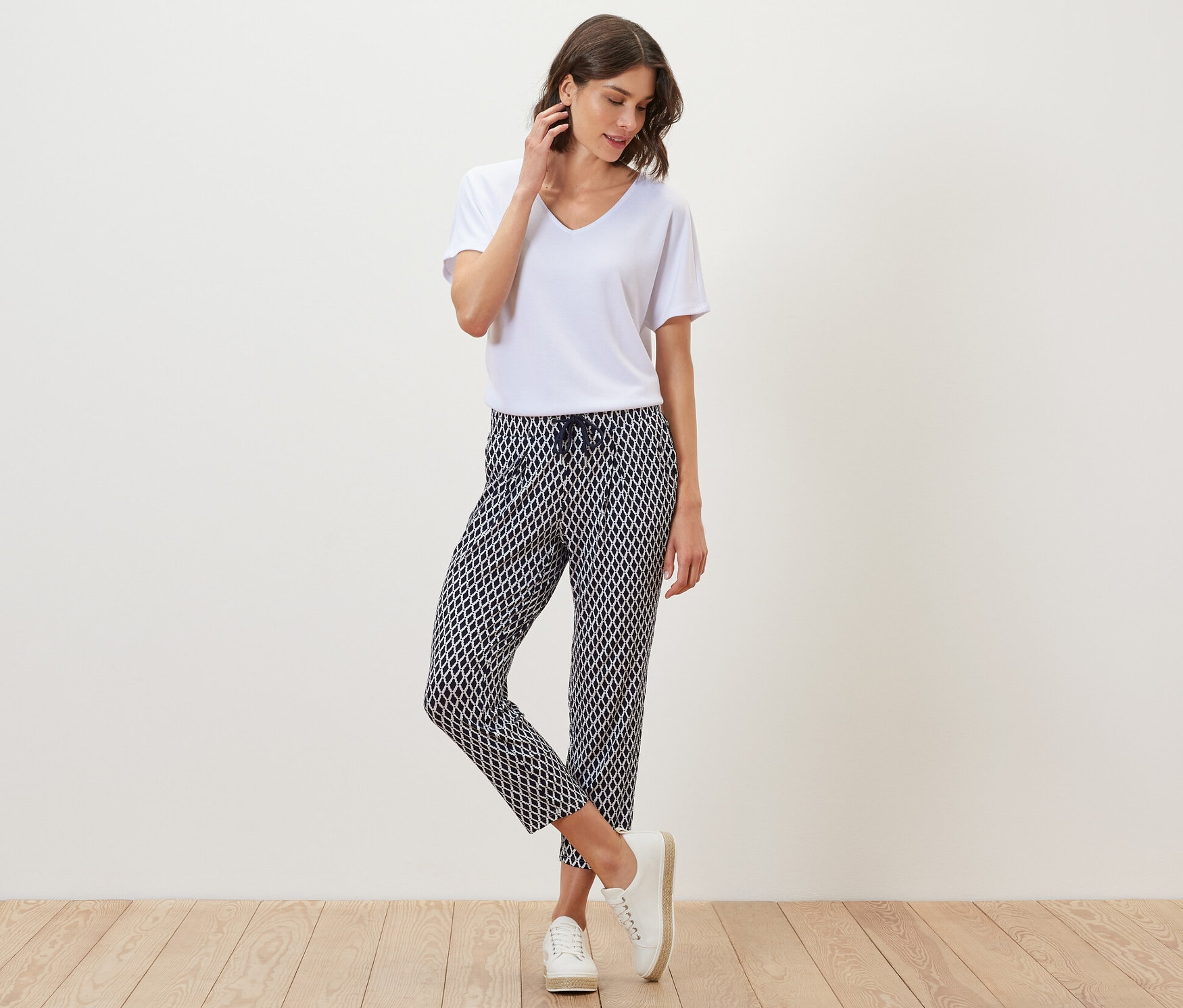 Frau posiert in weißem T-Shirt und bedruckter Jerseyhose.
