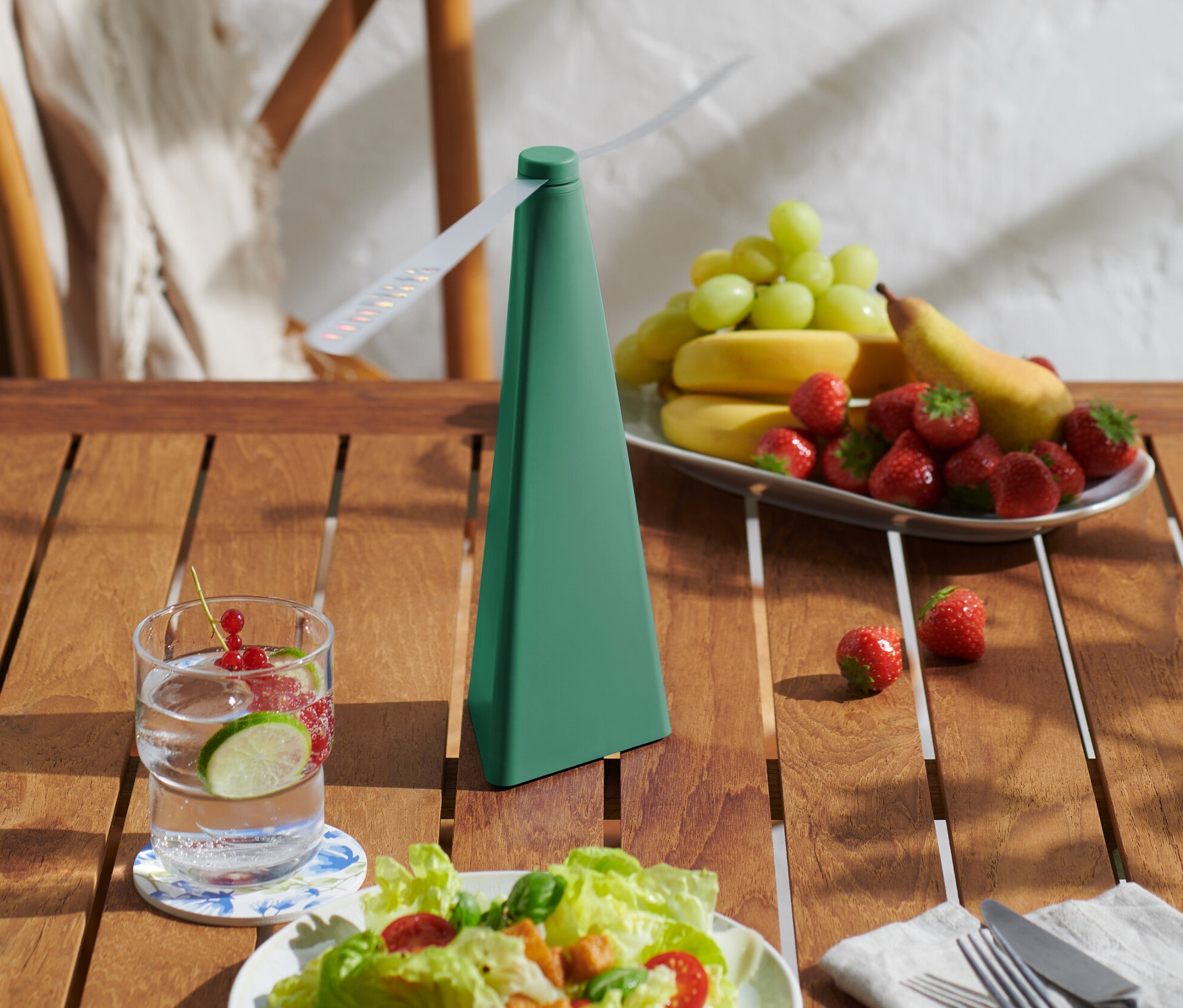 Auf einem Tisch stehen ein Fliegenwedler, ein Glas Wasser mit Früchten und eine Obstplatte.