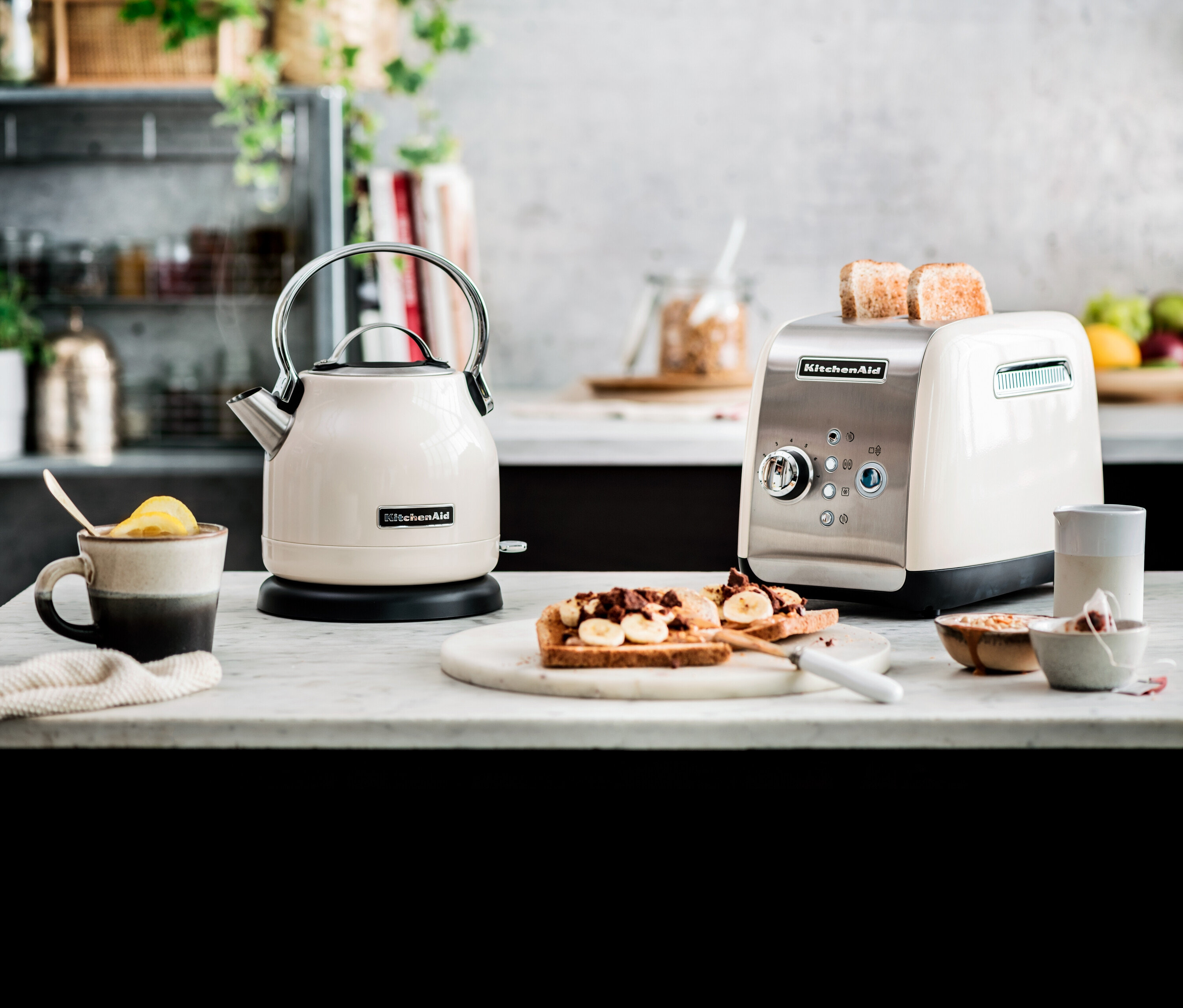 Ein cremefarbener KitchenAid Wasserkocher und Toaster auf einer Küchentheke mit Bananen-Toast.