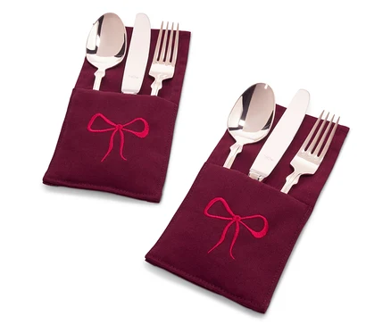 Zwei Bestecksets in weinroten Stoffhüllen mit roter Schleifenstickerei.