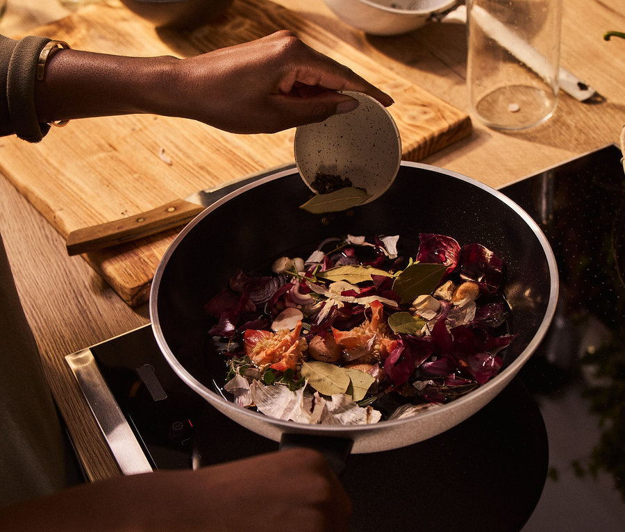 Frau gibt Gewürze in eine Pfanne mit Gemüse auf dem Herd.
