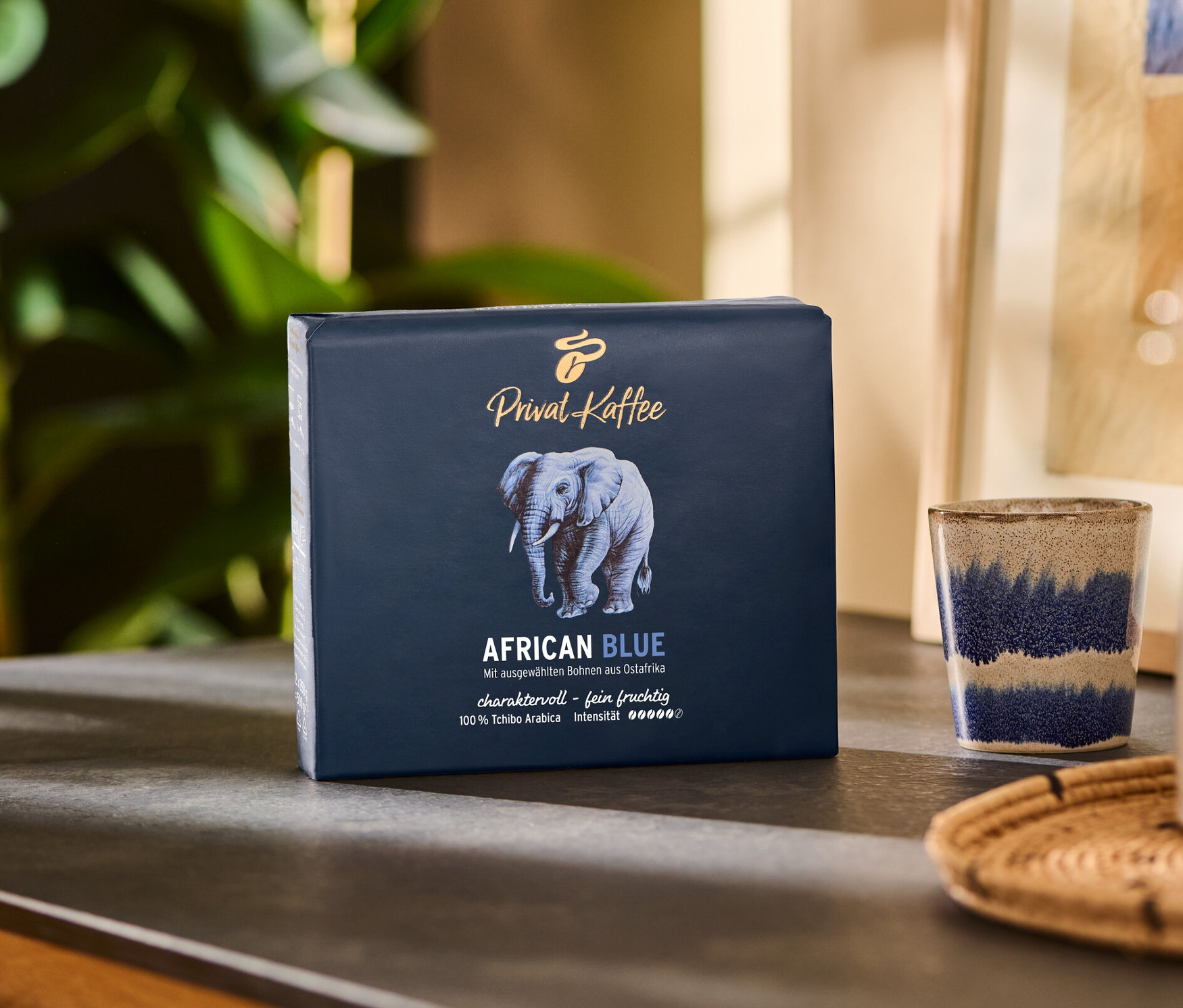 Eine Packung Privat Kaffee African Blue - 2x 250 g Gemahlen steht auf einem Tisch neben einer Tasse und einem Krug.