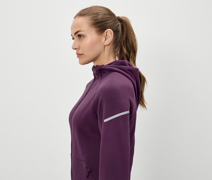 Profil einer Frau mit braunen Haaren, die zu einem Pferdeschwanz zusammengebunden sind, sie trägt einen violetten Kapuzenpullover.