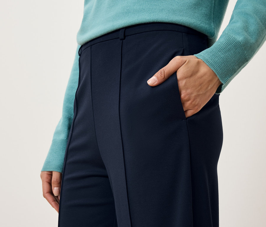 Detailaufnahme einer Frau, die blaue Hosen und einen Pullover trägt und ihre Hand in der Hosentasche hat.