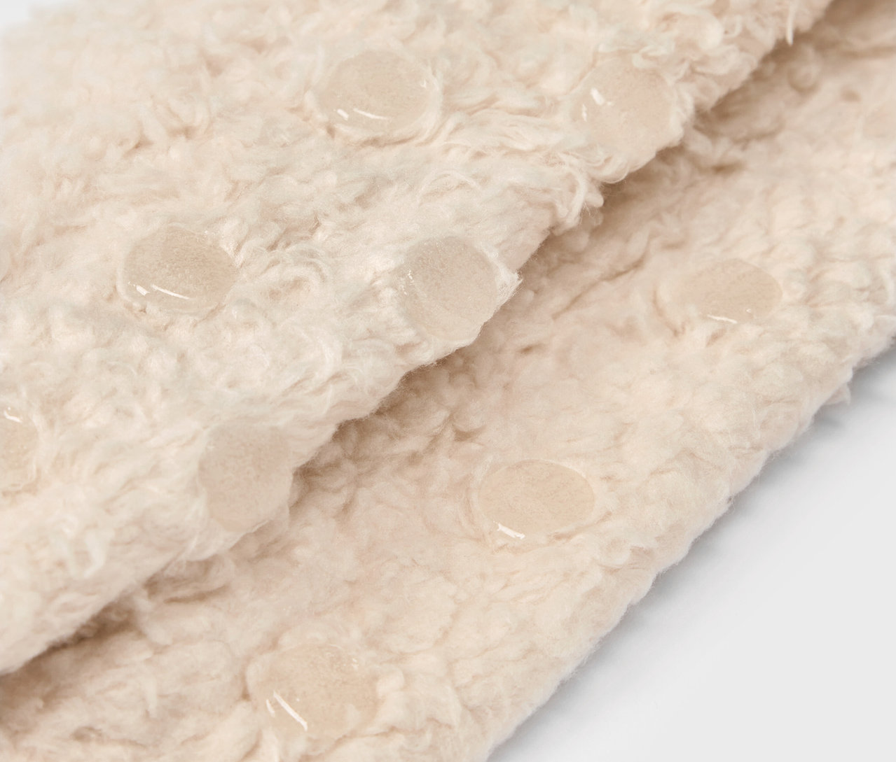 Detailaufnahme eines beigen, flauschigen Stoffes mit Anti-Rutsch-Noppen.