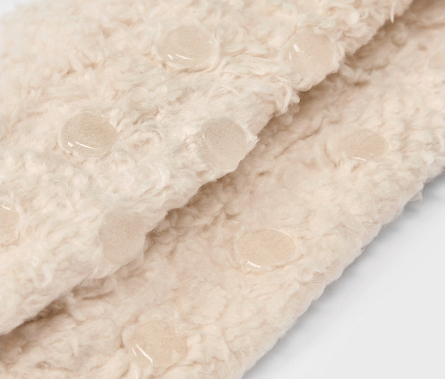 Detailaufnahme eines beigen, flauschigen Stoffes mit Anti-Rutsch-Noppen.