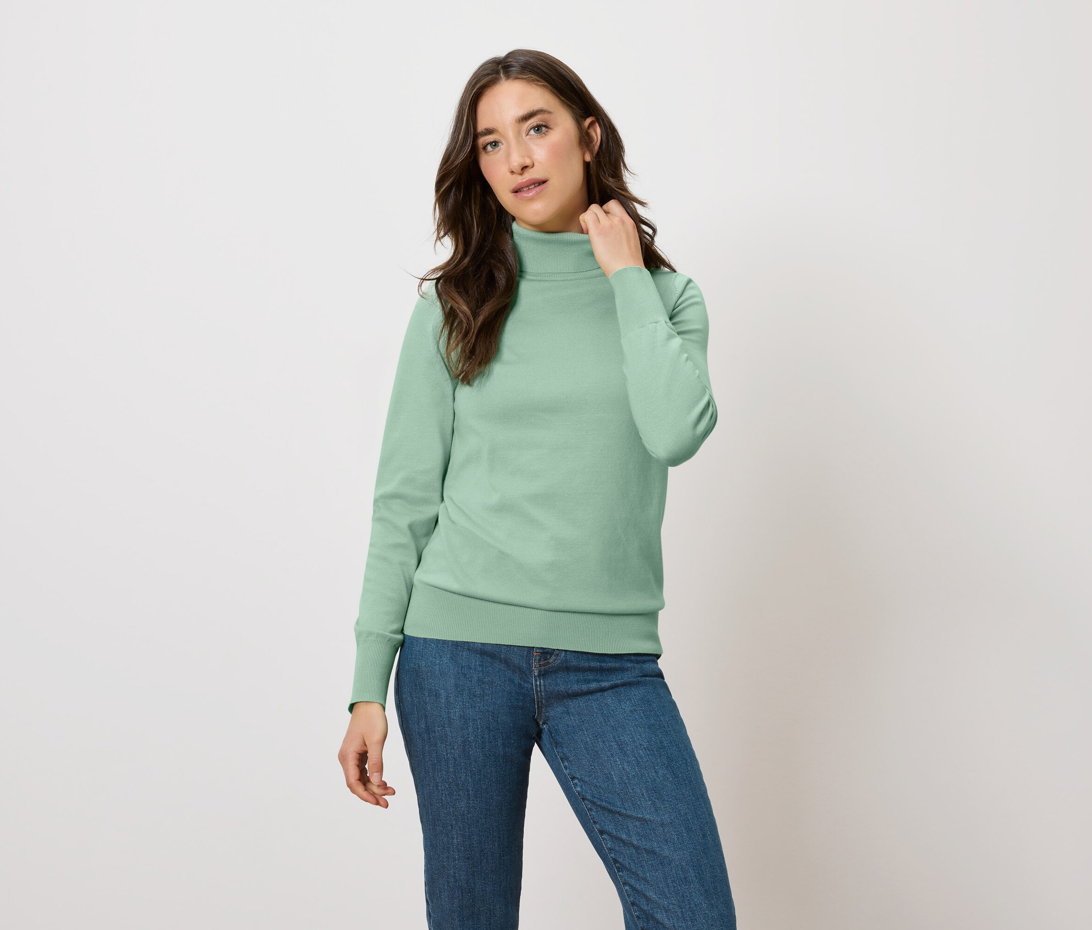 Frau posiert in einem grünen Rollkragenpullover und blauen Jeans.