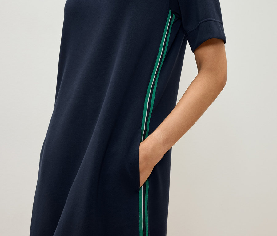 Frau hat die Hand in der Tasche eines dunkelblauen, kurzärmeligen Kleides mit grünem und weißem Streifen.