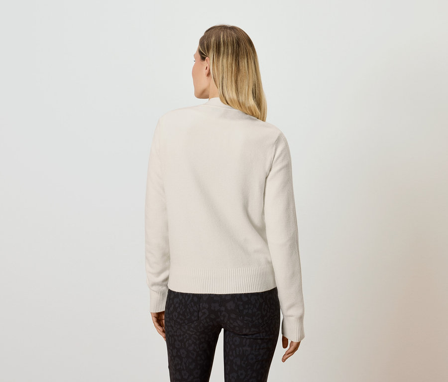 Rückansicht einer blonden Frau in einem cremefarbenen Pullover und schwarzen Leggings.