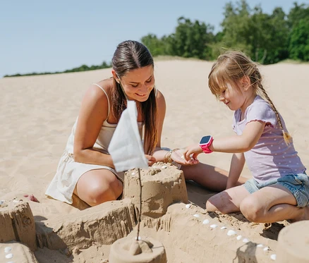 Frau und Mädchen bauen eine Sandburg am Strand. Das Mädchen trägt eine rosa Kids Watch Xplora XGO3.