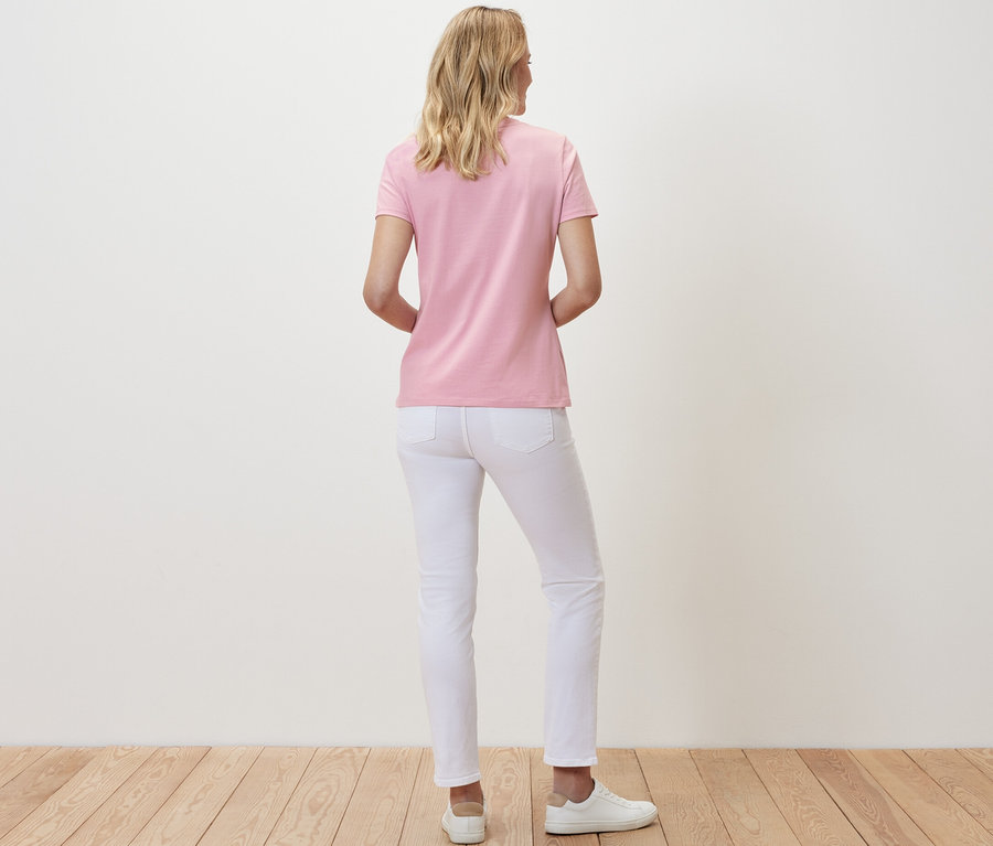 Eine Frau steht mit dem Rücken zur Kamera und trägt ein rosafarbenes Basic T-Shirt und weiße Jeans.