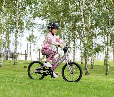 Ein Mädchen fährt mit einem PUKY LS-PRO 18 Fahrrad in Pearl Pink auf einer Wiese in einem Park.
