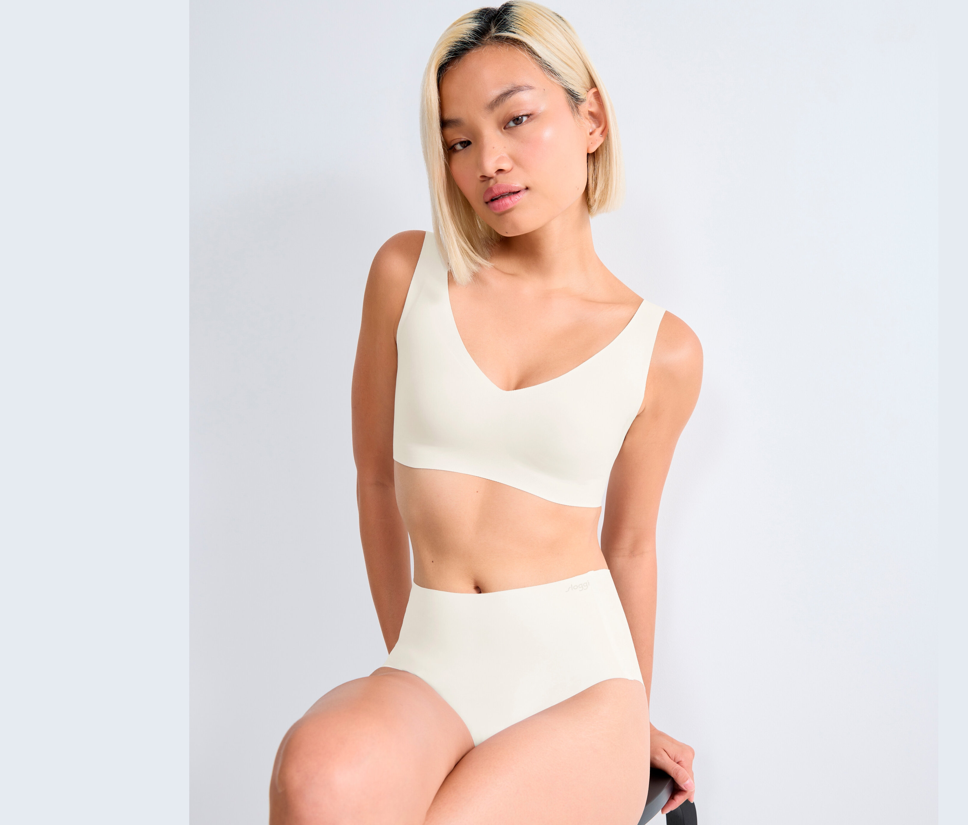 Frau sitzt und trägt ein weißes sloggi ZERO Feel 2.0 Bralette und Höschen.