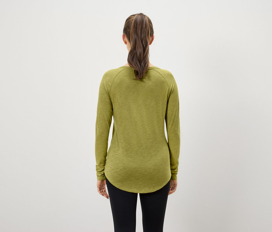 Rückansicht einer Frau mit braunen Haaren, die zu einem Pferdeschwanz zusammengebunden sind. Sie trägt ein olivgrünes Langarmshirt und schwarze Leggings.