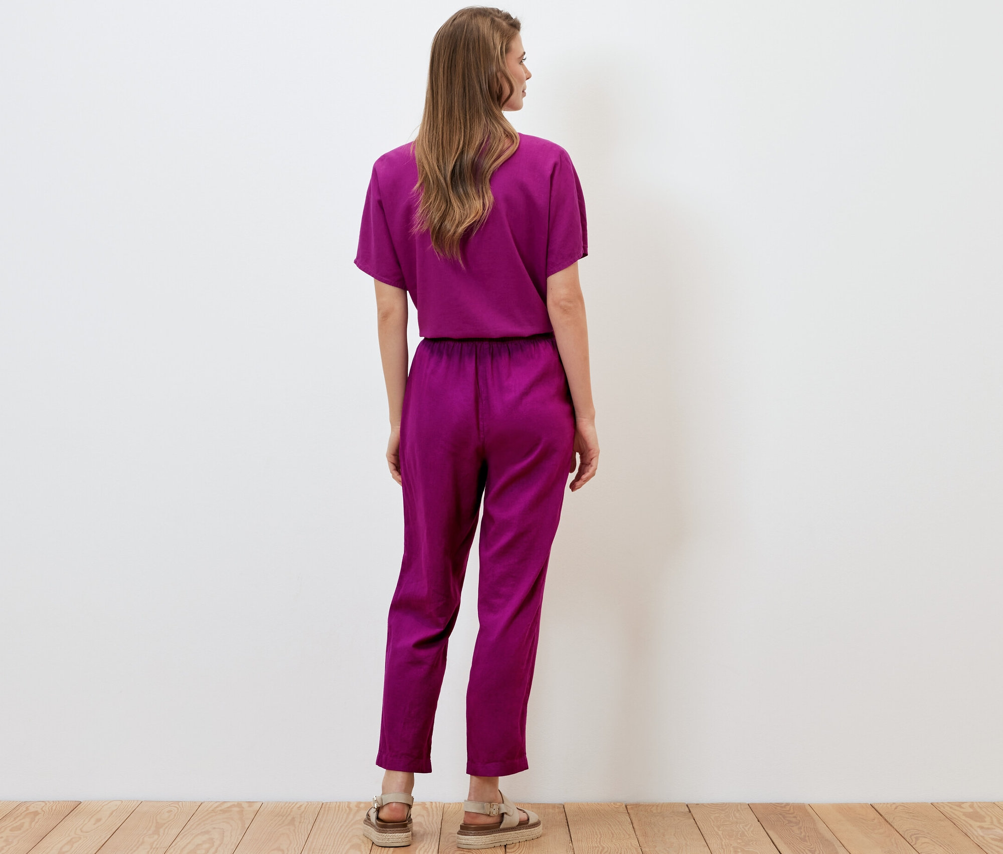 Frau steht mit dem Rücken zur Kamera und trägt eine Leinenhose in Beere.