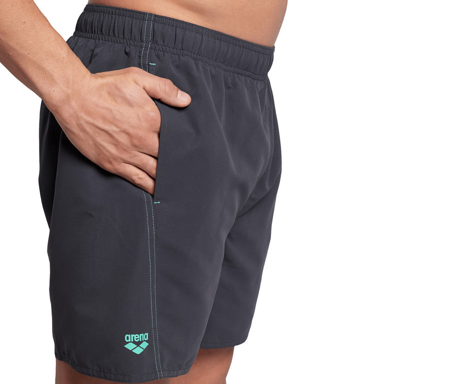 Mann hat Hand in Tasche von grauer Badeshorts.