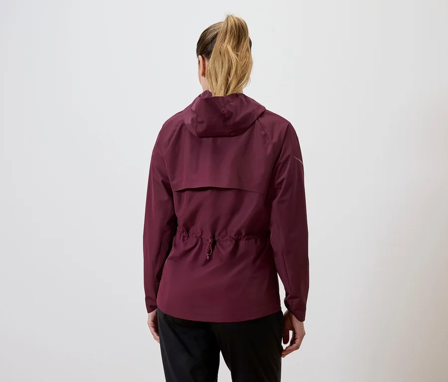 Rückansicht einer Frau mit blondem Pferdeschwanz, die eine weinrote Jacke mit Kapuze und Kordelzug an der Taille und eine schwarze Hose trägt.