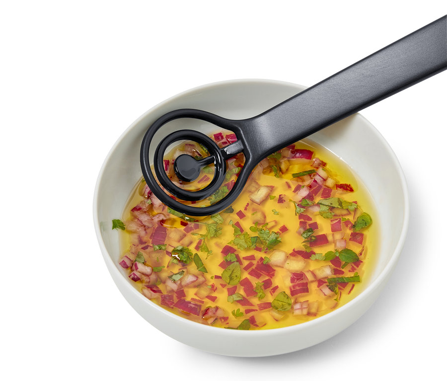 In einer weißen Schüssel befindet sich eine Vinaigrette mit gehackten roten Zwiebeln und Kräutern, die mit einem schwarzen Schneebesen verrührt wird.