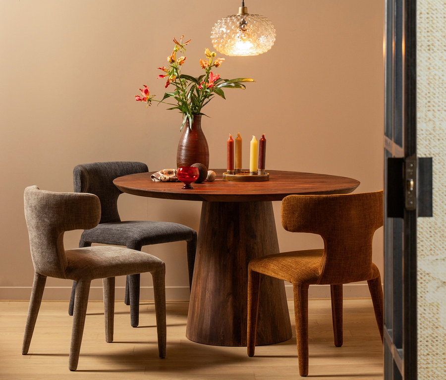 Drei »Permit« Stühle von WOOOD im 2er-Set in Zimtfarben stehen um einen runden Holztisch mit Blumen, Kerzen und Dekorationen.