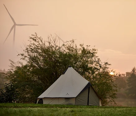 Ein Zelt steht auf einer Wiese, im Hintergrund Windräder im Morgenlicht.