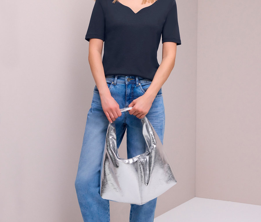 Frau in Street One Kurzarmshirt in Navy, hellblauen Jeans und silbernen Sneakern, die eine silberne Tasche hält.