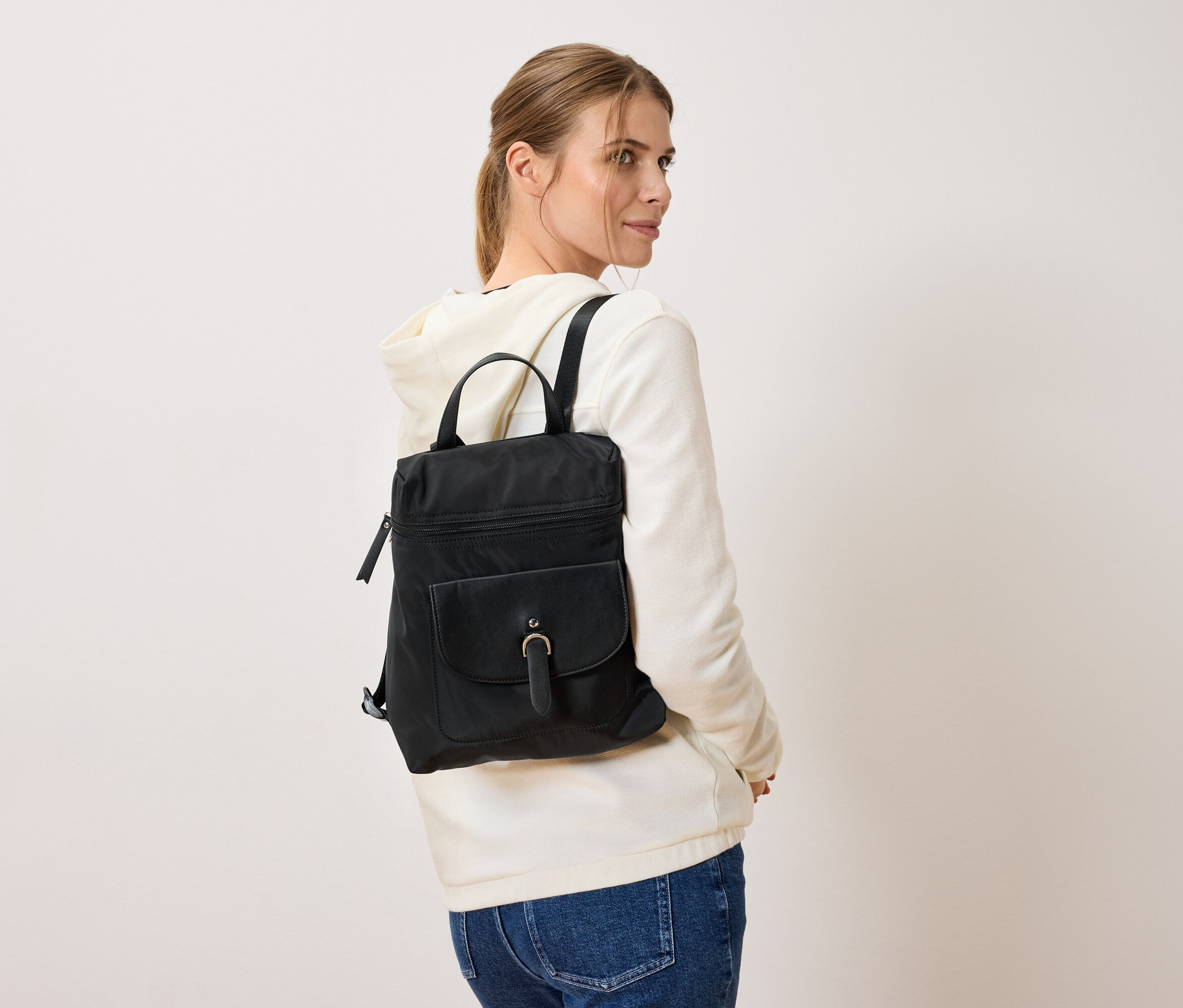 Frau mit schwarzem Rucksack, stehend vor einem weißen Hintergrund.