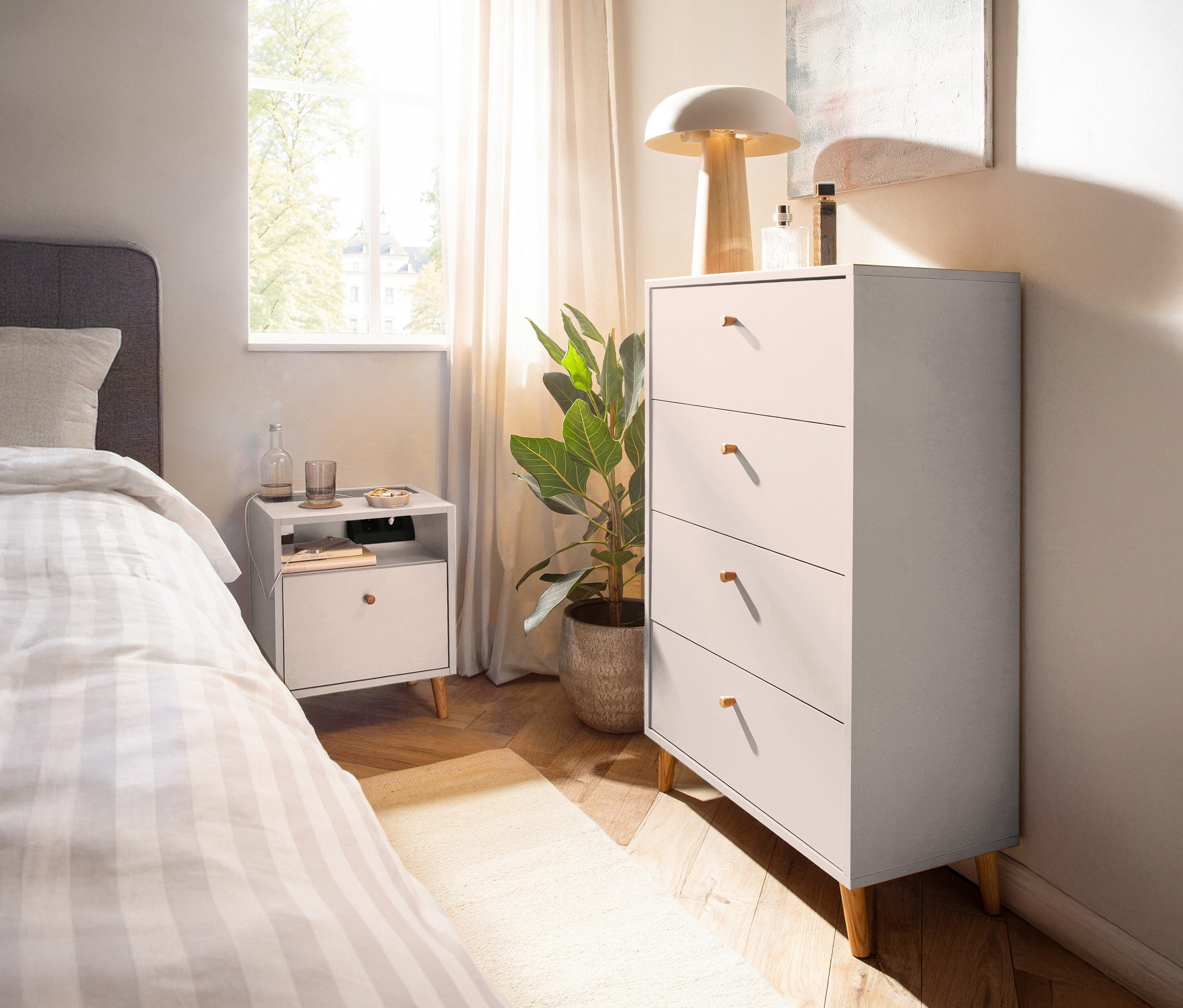 Schlafzimmer mit einem weißen Nachttisch »Bjarne« mit Ladefunktion neben einem Bett und einer Kommode.