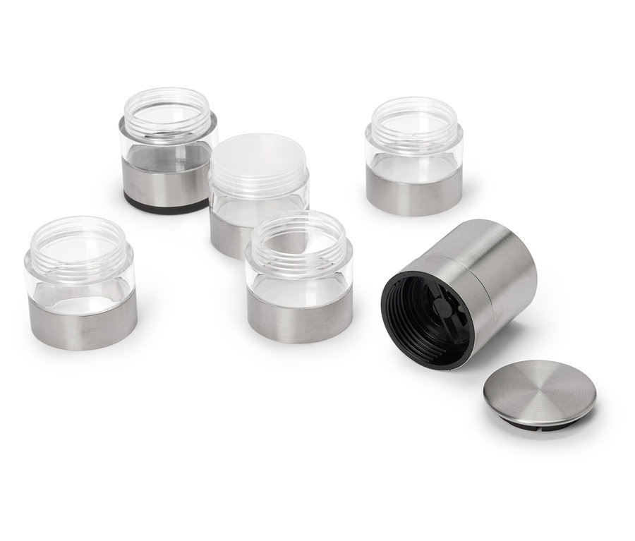 Sechs Gewürzgläser, teils mit Metalldeckel, teils offen, liegen auf einem weißen Untergrund.