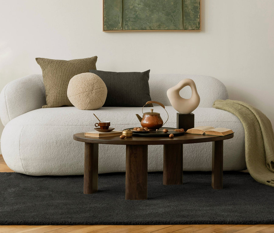 Ein anthrazitfarbener Teppich »Jane« liegt unter einem Wohnzimmer mit Sofa, Kissen und einem Couchtisch.