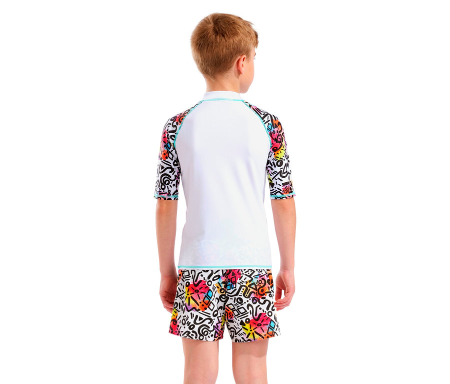 Junge von hinten, trägt ein weißes Rash Guard Oberteil mit bunten Ärmeln und farbigen Shorts mit grafischem Muster.