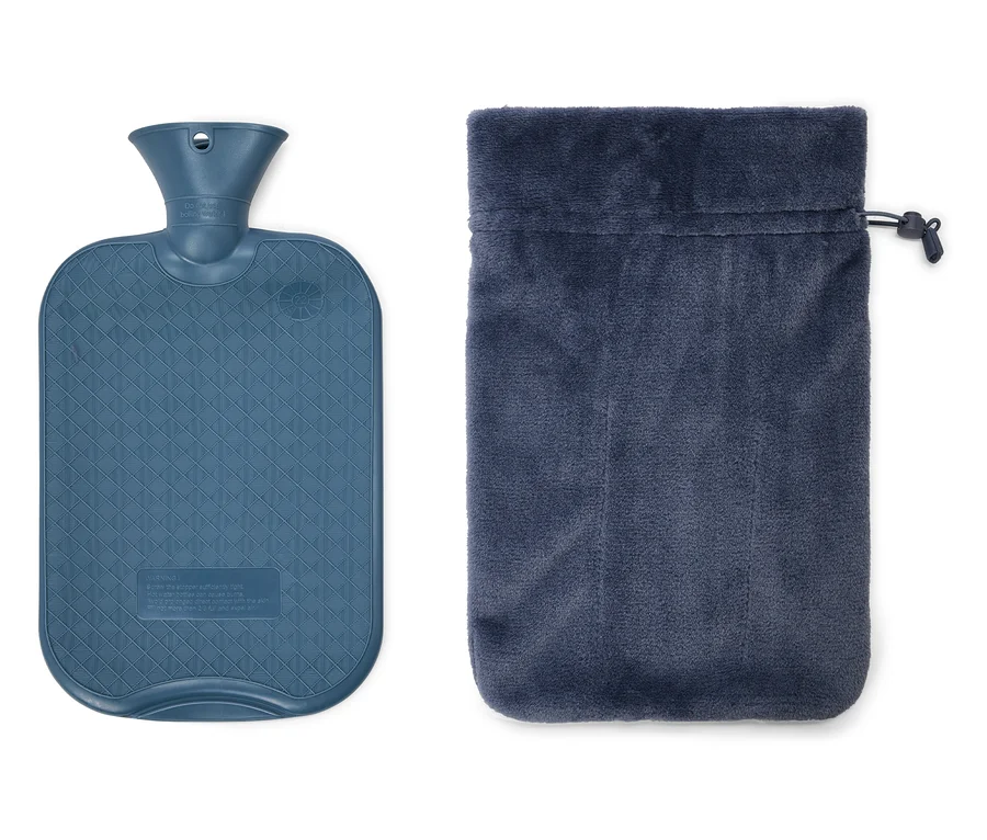Eine blaue Wärmflasche mit Rautenmuster liegt neben einem blauen Samtbeutel mit Kordelzug.