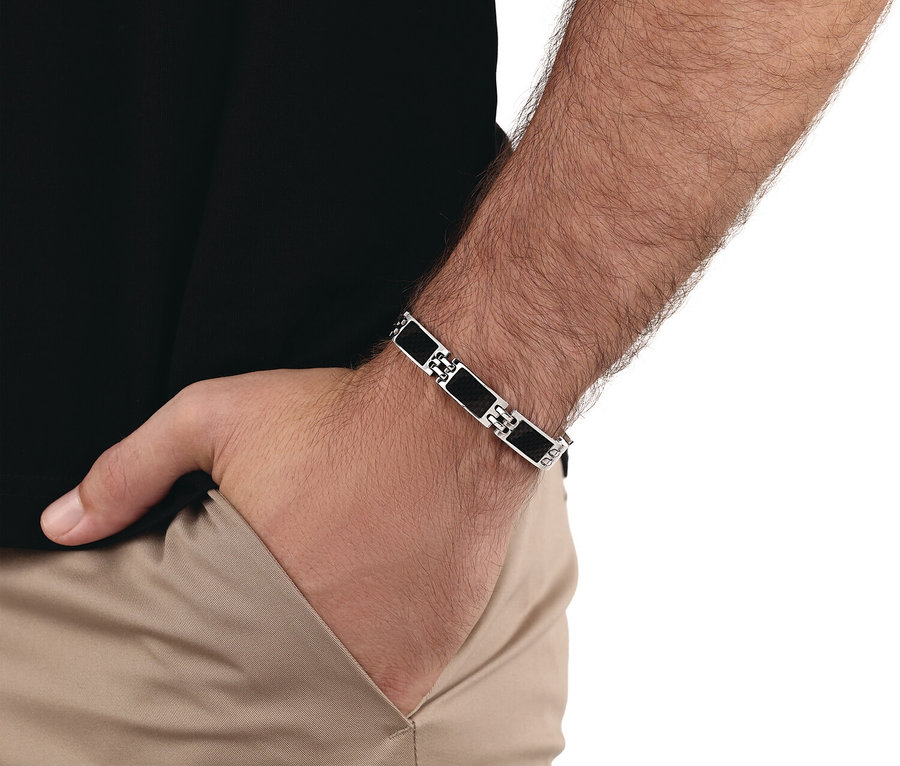Nahaufnahme eines Mannes, der ein silbernes und schwarzes Gliederarmband am Handgelenk trägt, während er seine Hand in einer Hosentasche hat.
