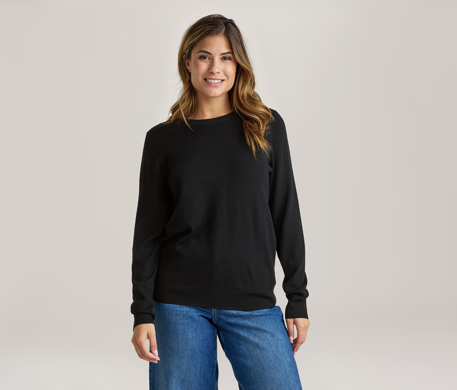 Lächelnde Frau in schwarzem Langarmshirt und blauen Jeans.